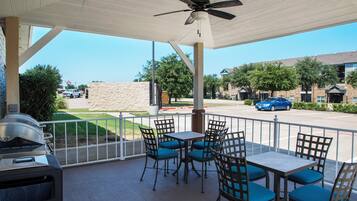An outdoor patio with tables and chairs, a ceiling fan, and a grill.