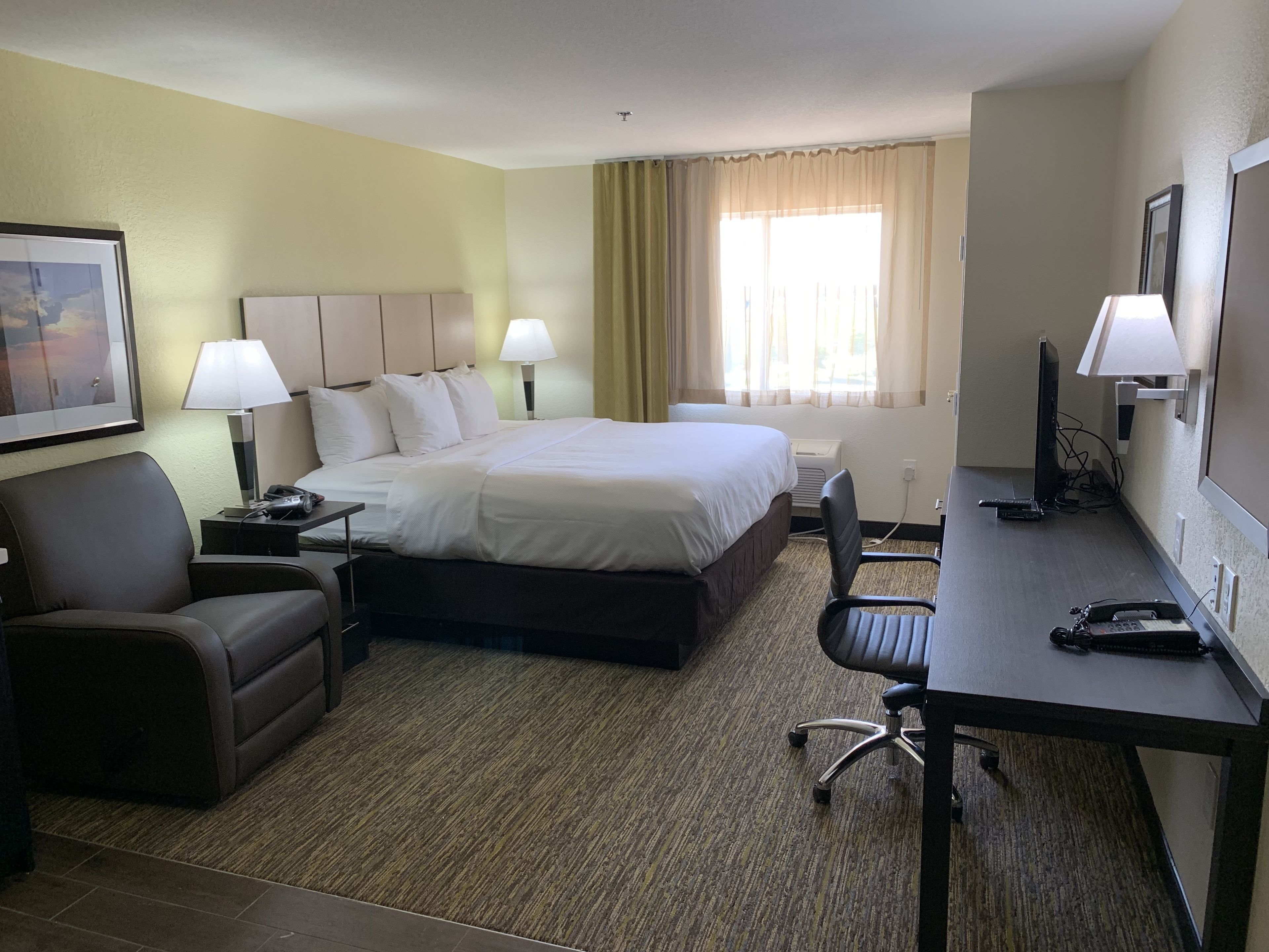 A hotel room with a bed, a desk, a chair, a couch, and a TV.