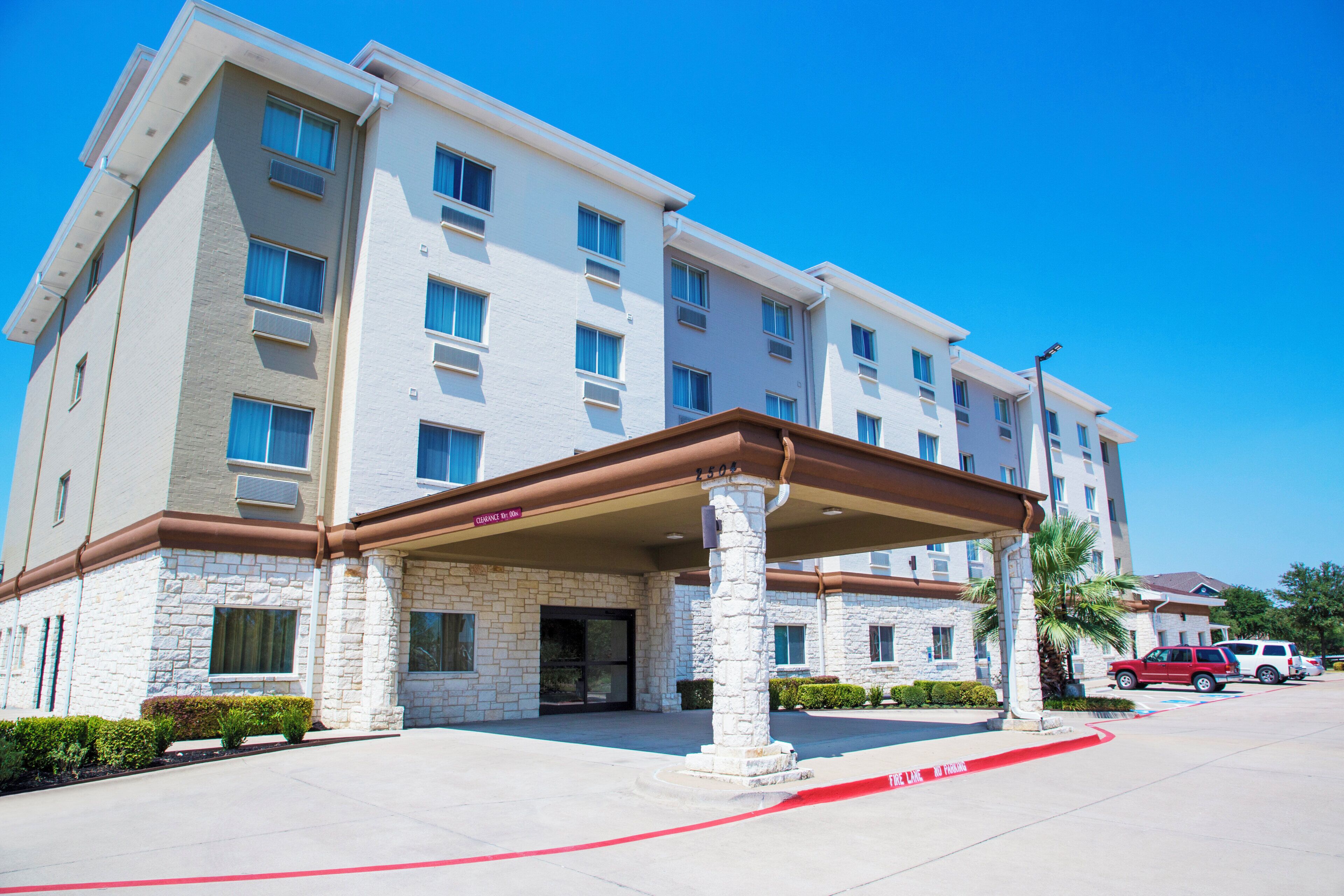 A multi-story hotel with a stone facade, a covered entrance, and a clear blue sky.