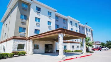 A multi-story hotel with a stone facade, a covered entrance, and a clear blue sky.