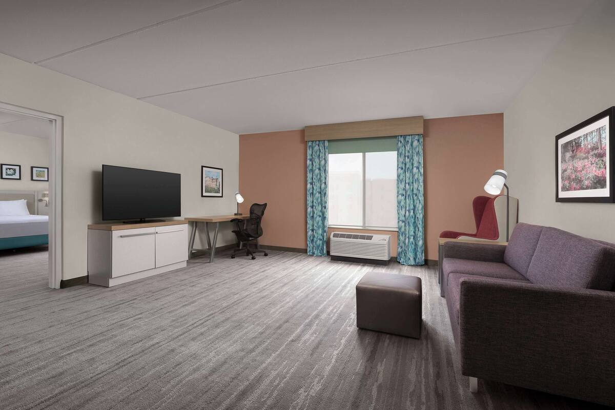A hotel room with a bed, a desk with a TV, a sofa, a chair, and a window with curtains.
