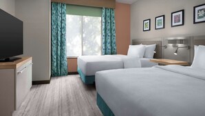 A hotel room with two beds, a TV, a desk, and a window with curtains.