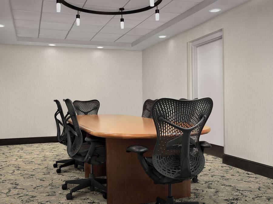 A conference room with a wooden table and black mesh chairs, white walls, and a patterned carpet.