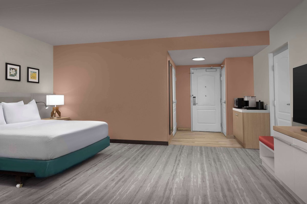 A hotel room with a bed, a desk, a TV, and a kitchenette.