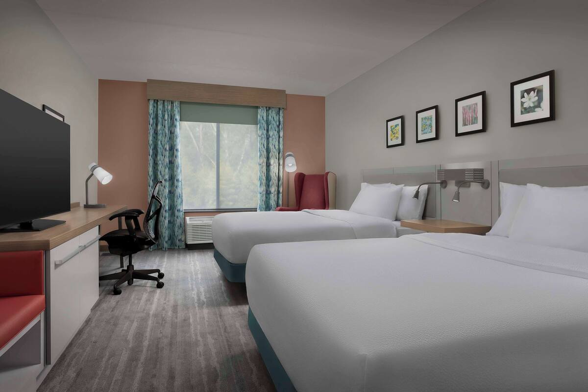 A hotel room with two beds, a desk with a computer, a chair, a TV, and a window with curtains.