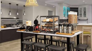 A modern kitchen with a central island, bar stools, a waffle maker, and a coffee station.
