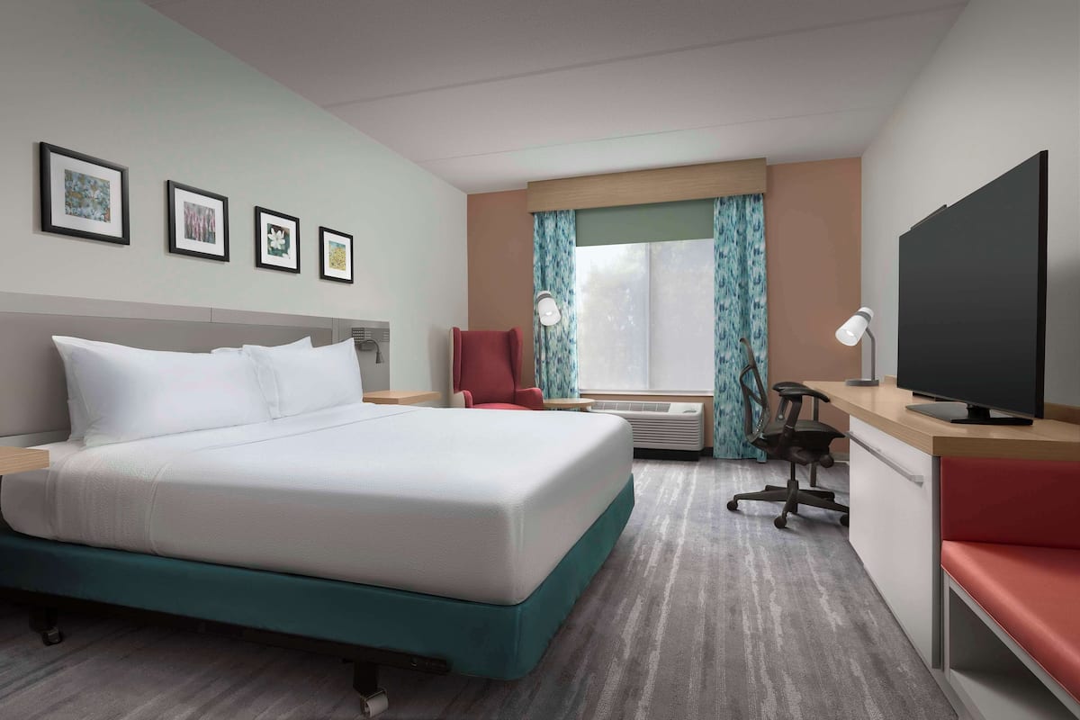 A hotel room with a bed, a desk, a chair, a television, and framed pictures on the wall.