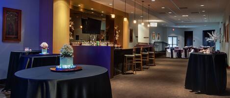 A hotel lobby with round tables, a bar area, and a seating arrangement.