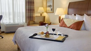 A hotel room with a neatly made bed, a dining table with a tray of food, a chair, and a lamp. - Hilton Garden Inn Cleveland East/Mayfield Village (Mayfield)