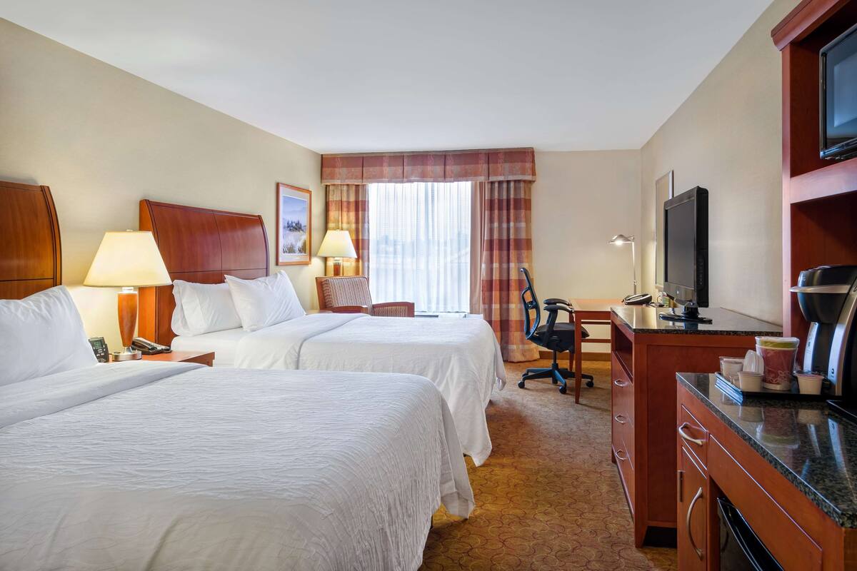 A hotel room with two beds, a desk, a television, and a kitchenette.