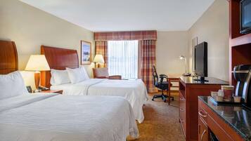 A hotel room with two beds, a desk, a television, and a kitchenette.