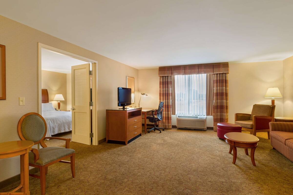 A hotel room with a bed, desk, chair, television, and a small table.