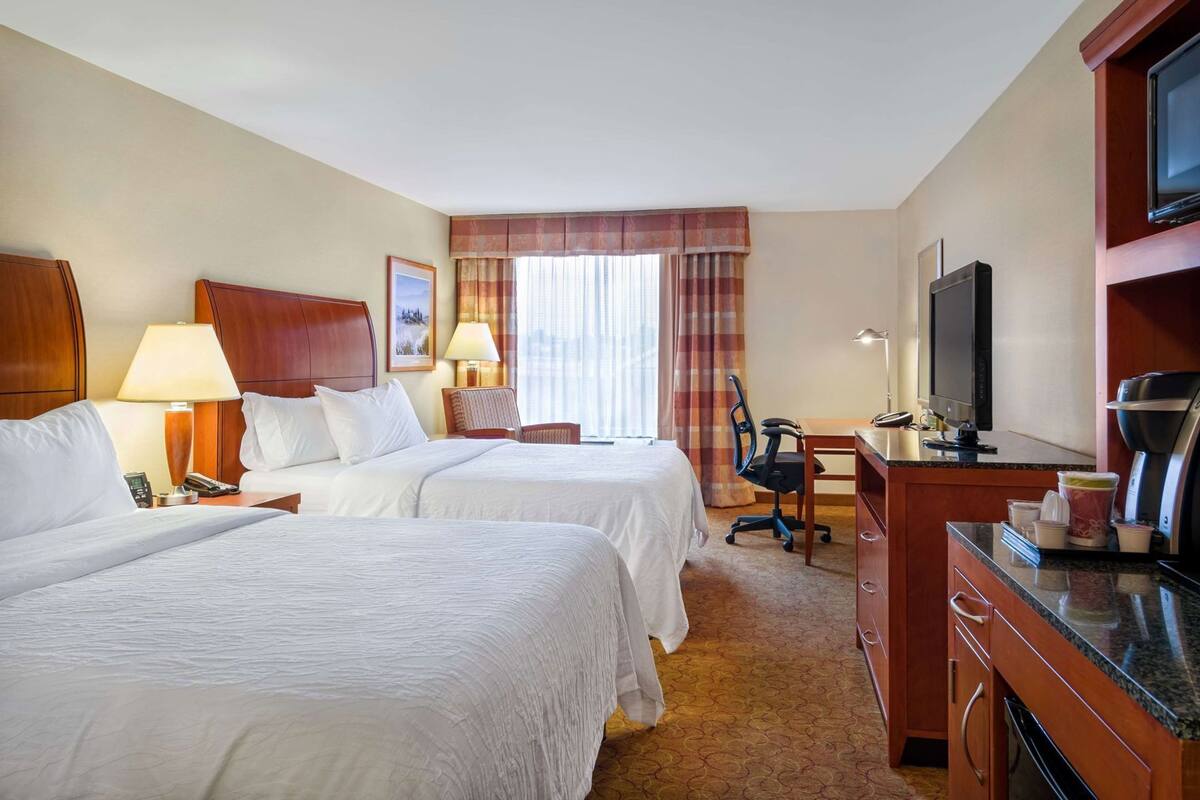 A hotel room with two beds, a desk, a chair, a TV, and a coffee maker.
