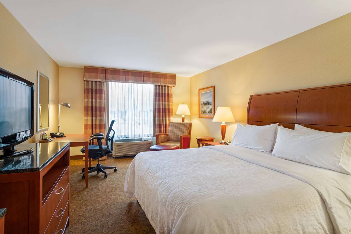 A hotel room with a bed, desk, chair, television, and lamps.