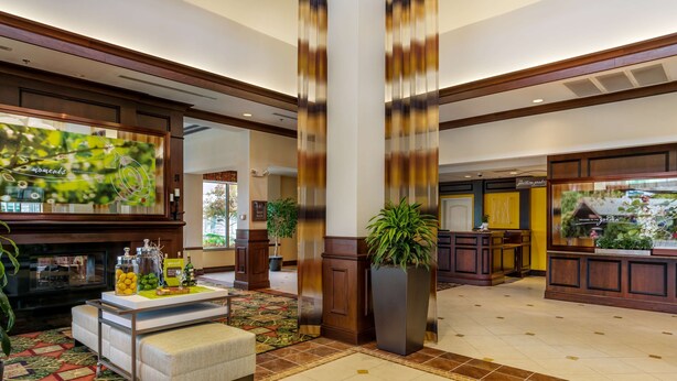 A spacious lobby with a reception desk, a large potted plant, and a decorative wall with a clock. - Hilton Garden Inn Cleveland East/Mayfield Village (Mayfield)