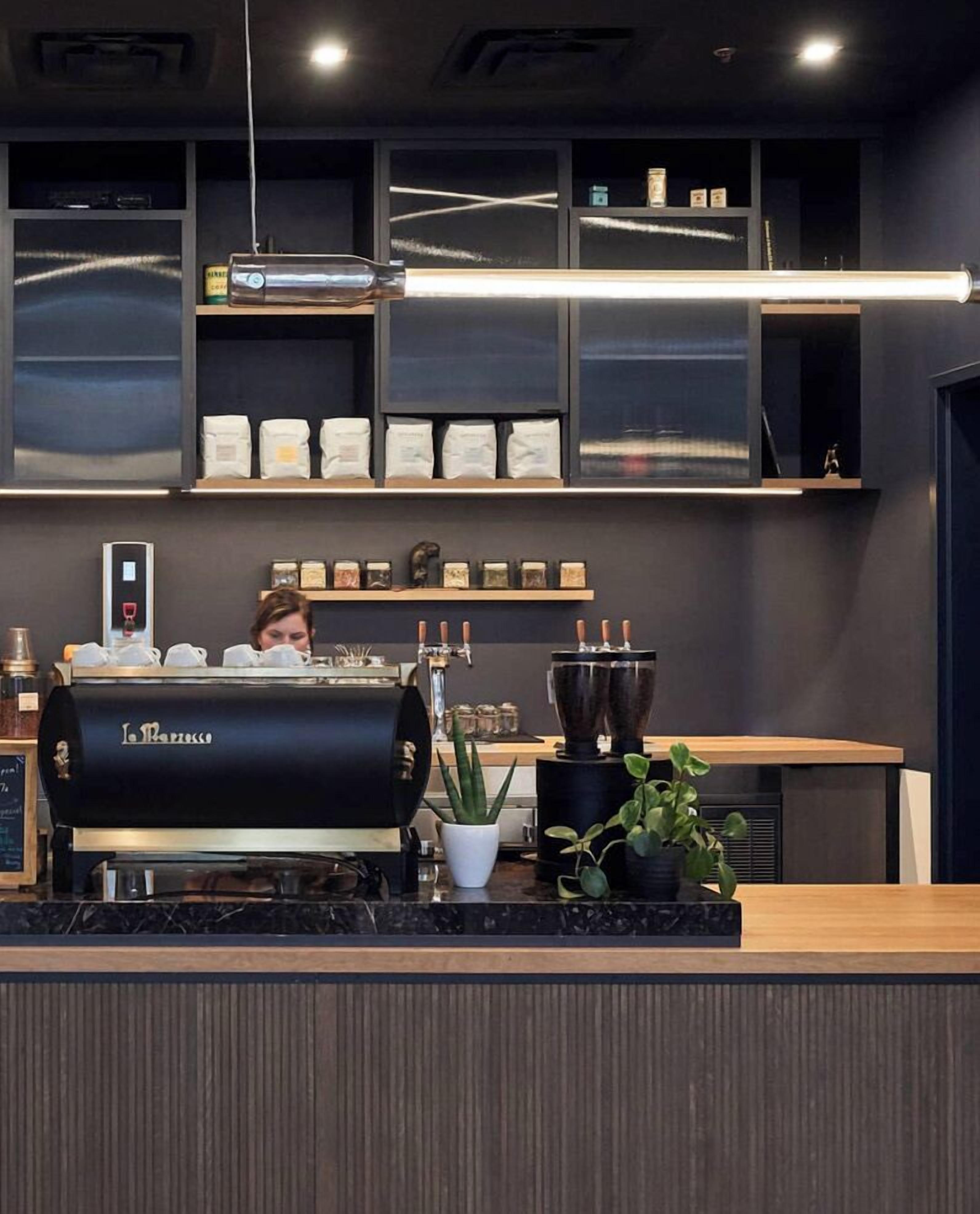 A coffee shop interior with a barista preparing drinks, a coffee machine, and shelves with coffee beans.