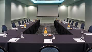 A conference room with a long table, chairs, a projector screen, and a carpeted floor.
