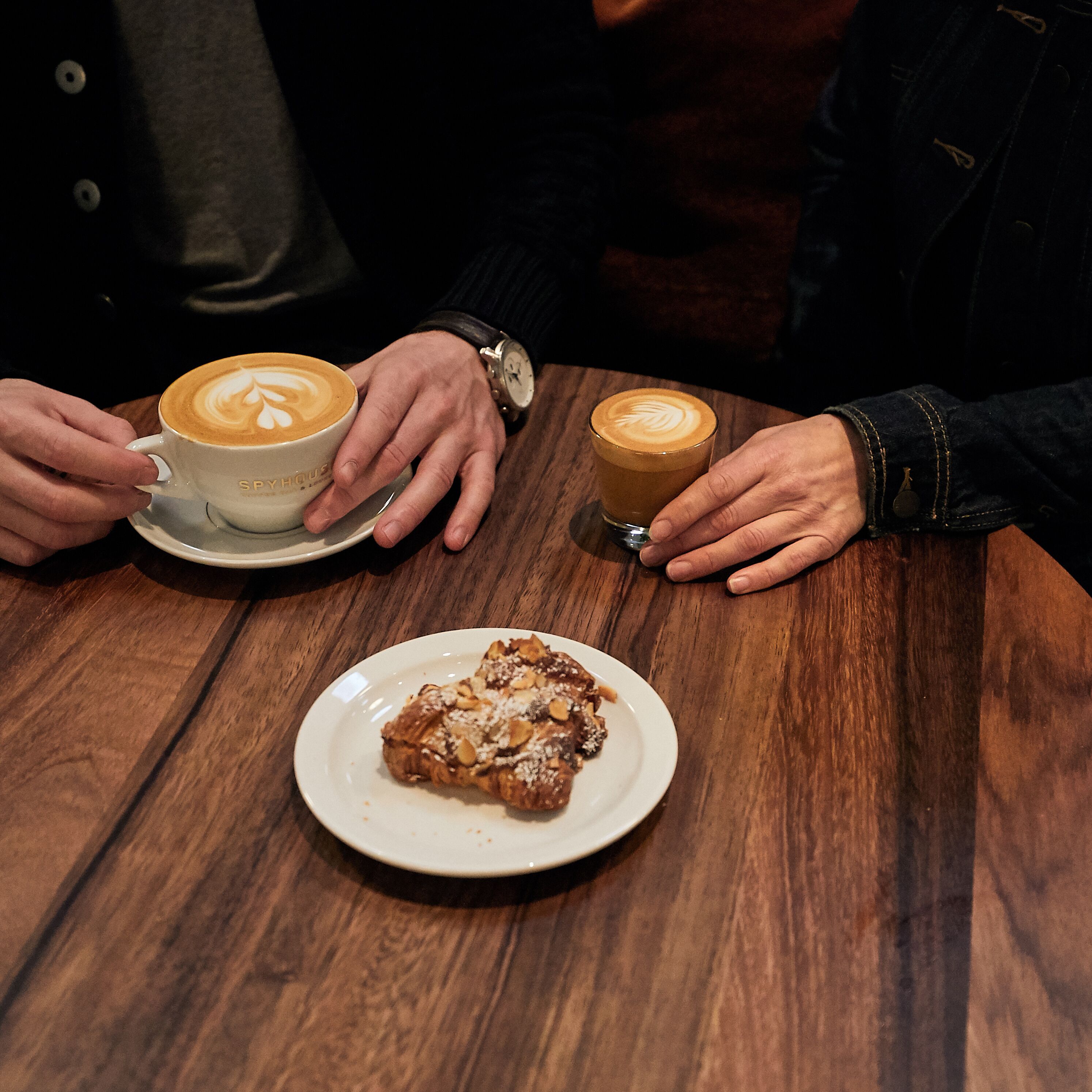 Een houten tafel met twee koffiekopjes en een bord eten.
