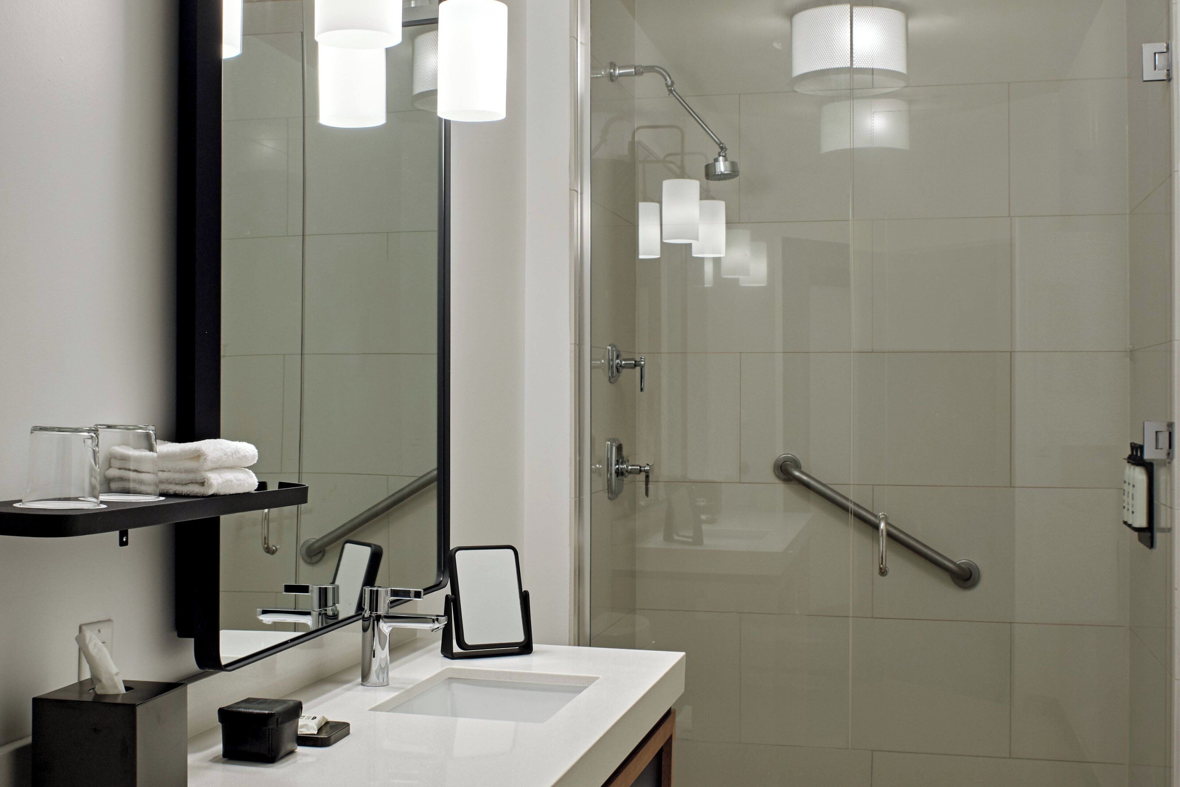 A modern bathroom with a large mirror, a sink, a glass shower enclosure, and a towel rack.