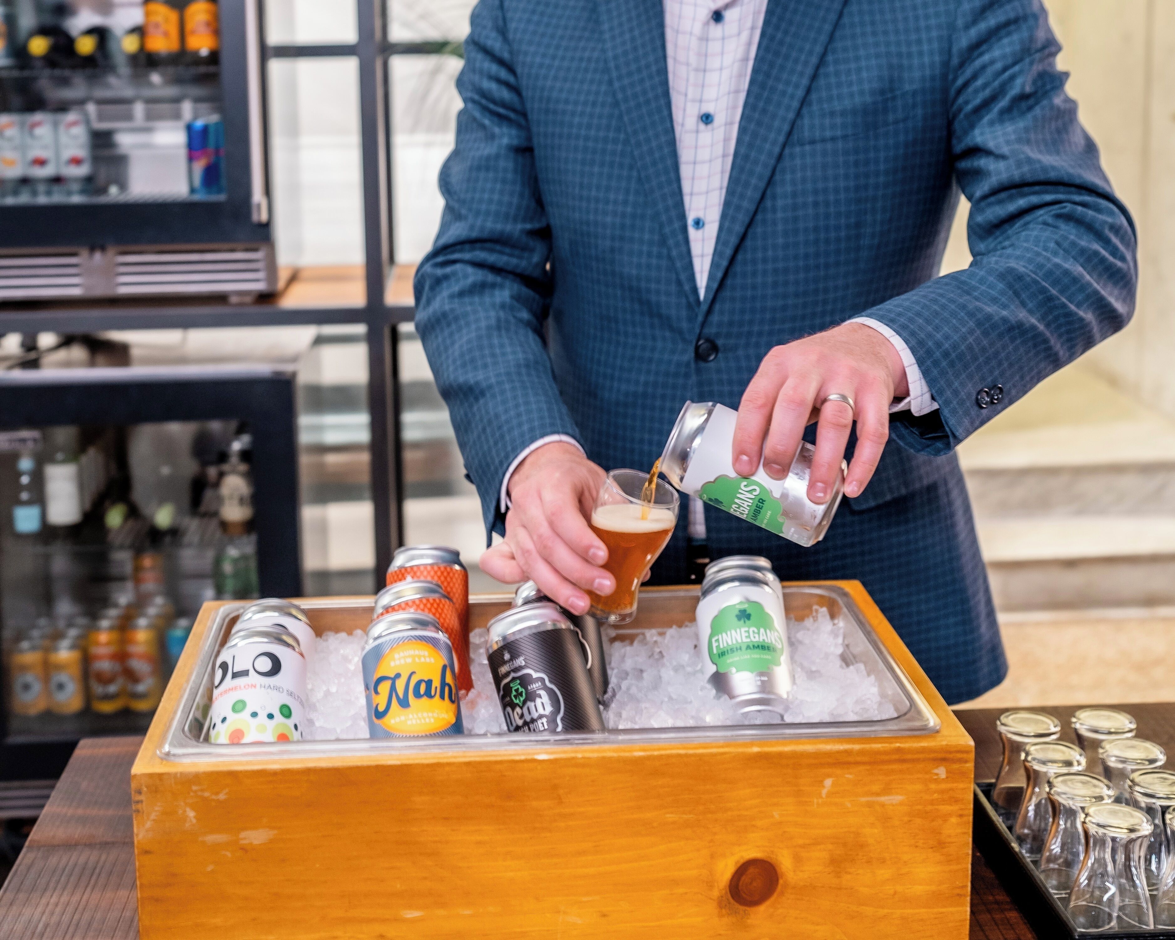 Une personne verse une boisson d’une canette dans un verre posé sur une surface en bois, avec des glaçons.