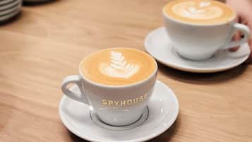 Two white cups of coffee with latte art on a wooden table, labeled "SPYHOUSE."