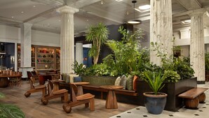 Eine großzügige Lobby mit Holzmöbeln, großen Topfpflanzen, Marmorsäulen und einem modernen Deckenstil.