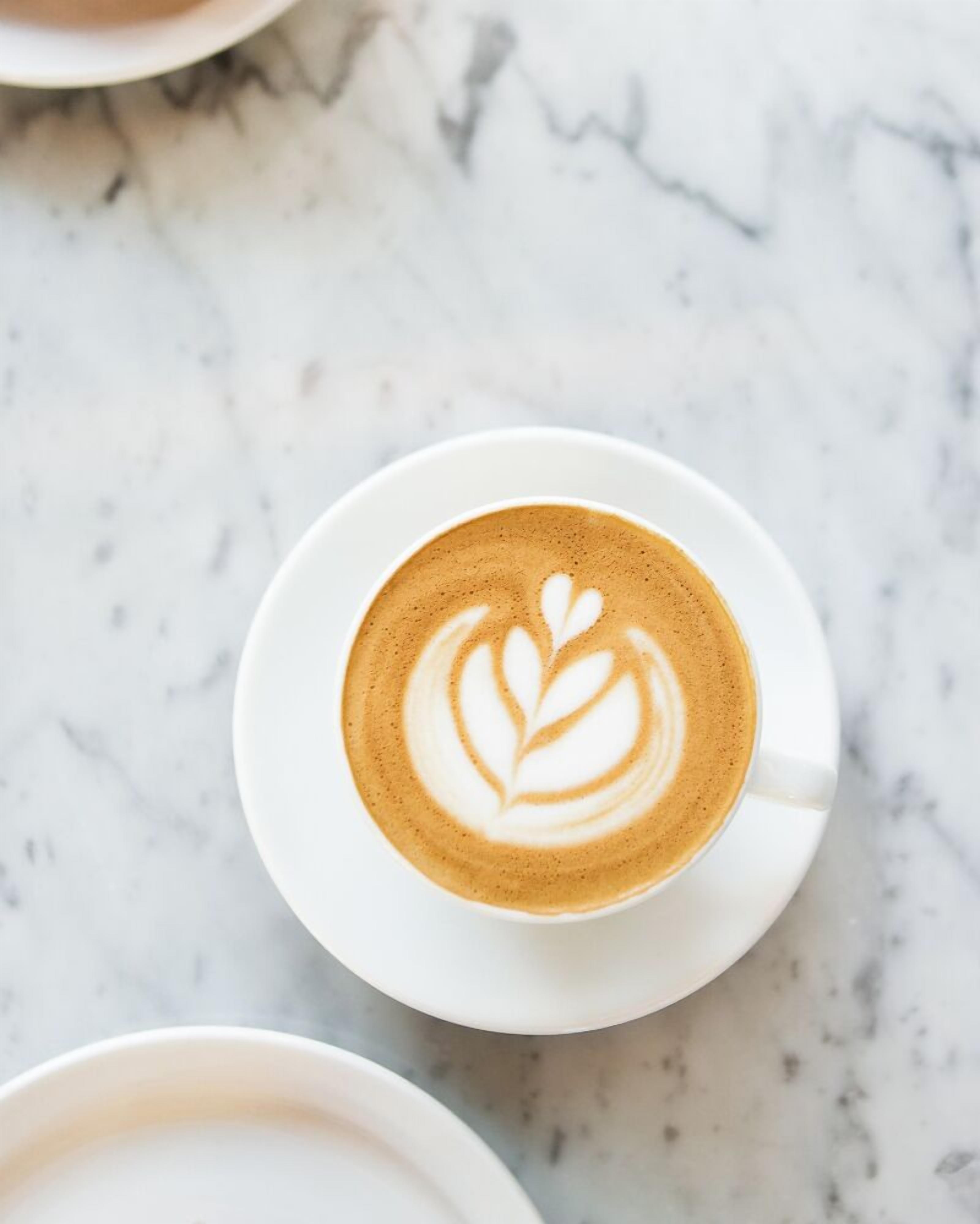 Una taza de café con arte de leche sobre un plato blanco, sobre una superficie de mármol.