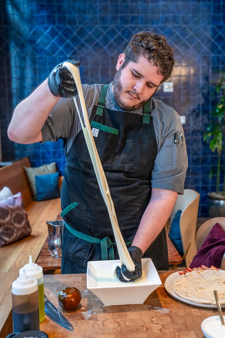 A person in a kitchen preparing food, with a cutting board, knife, and a bowl of sauce on the counter.