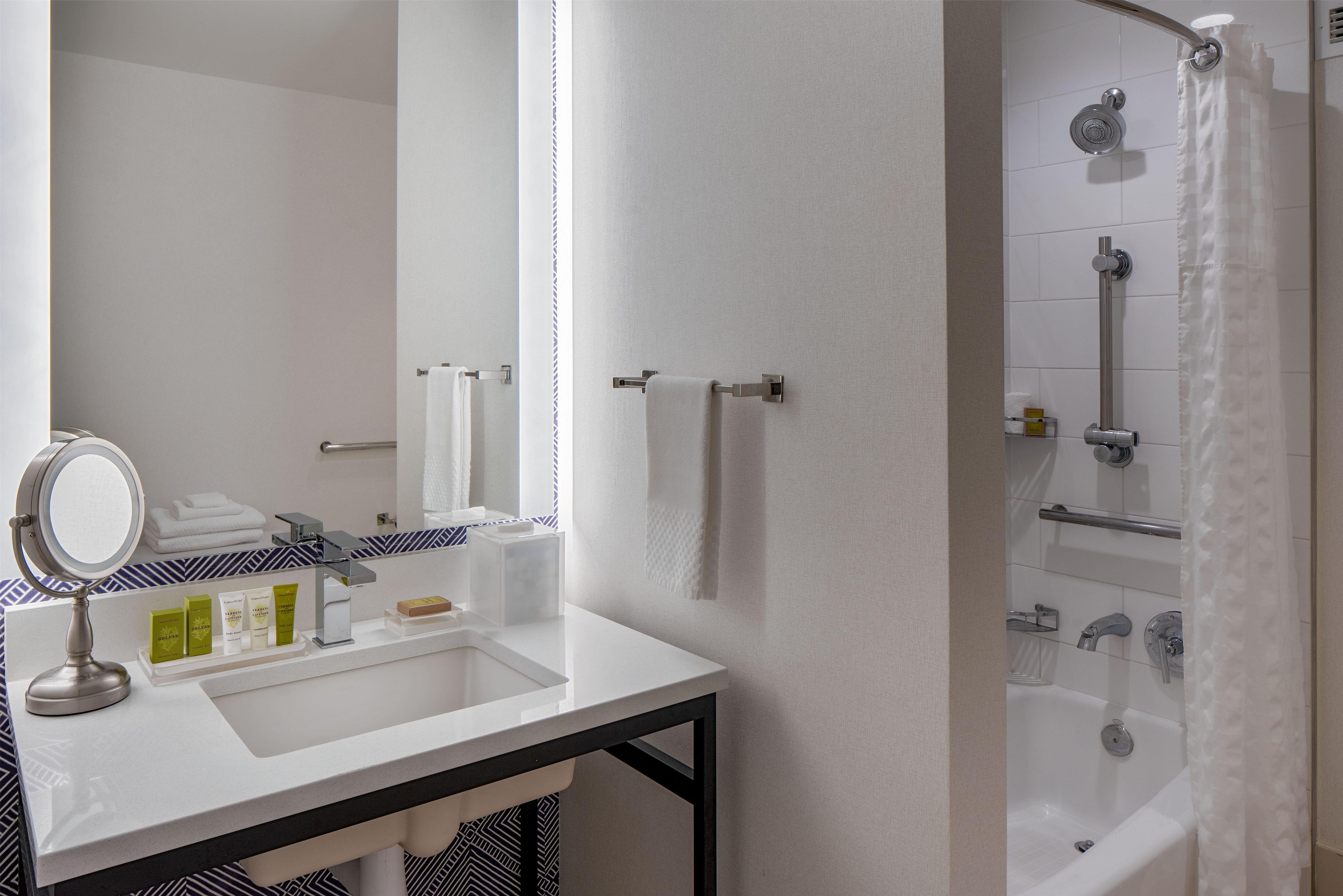 Un baño con lavamanos blanco, espejo y toallero.