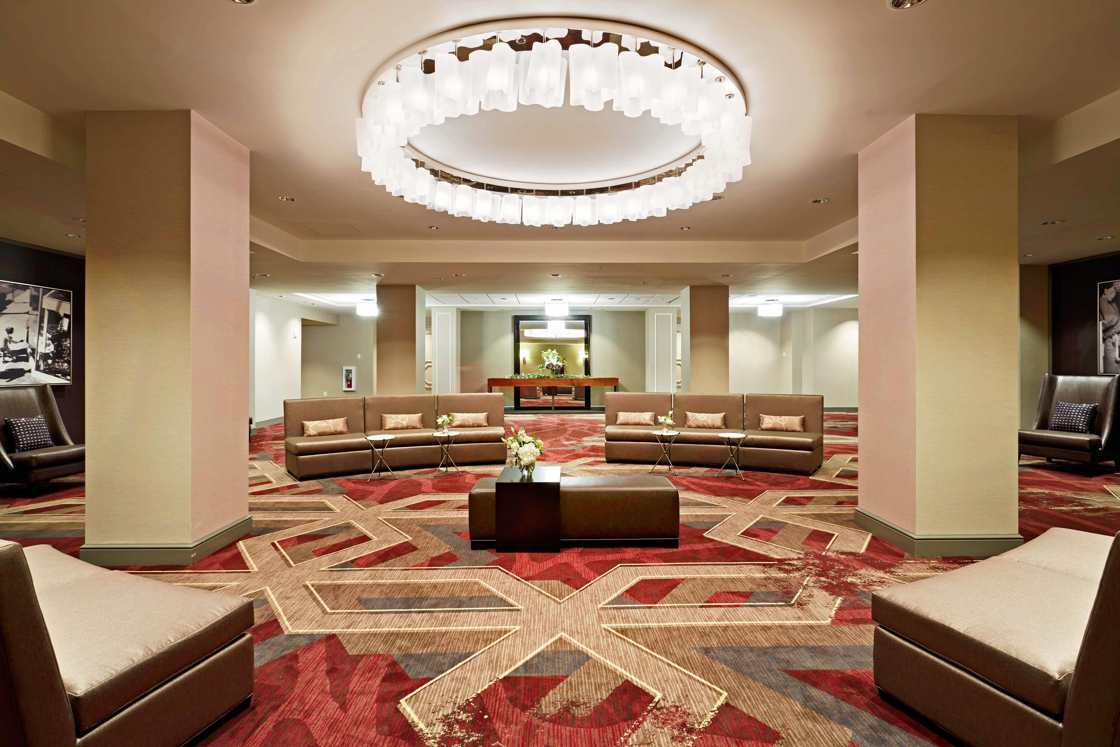 Un vestíbulo de hotel con un área de estar central, una araña y una alfombra estampada.