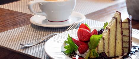 Un piattino con una fetta di torta, fragole e foglie di menta, accompagnato da una tazza di caffè su un sottopiatti.