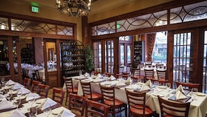 Un restaurante con varias mesas dispuestas para comer, sillas de madera y una estantería para vinos visible al fondo.