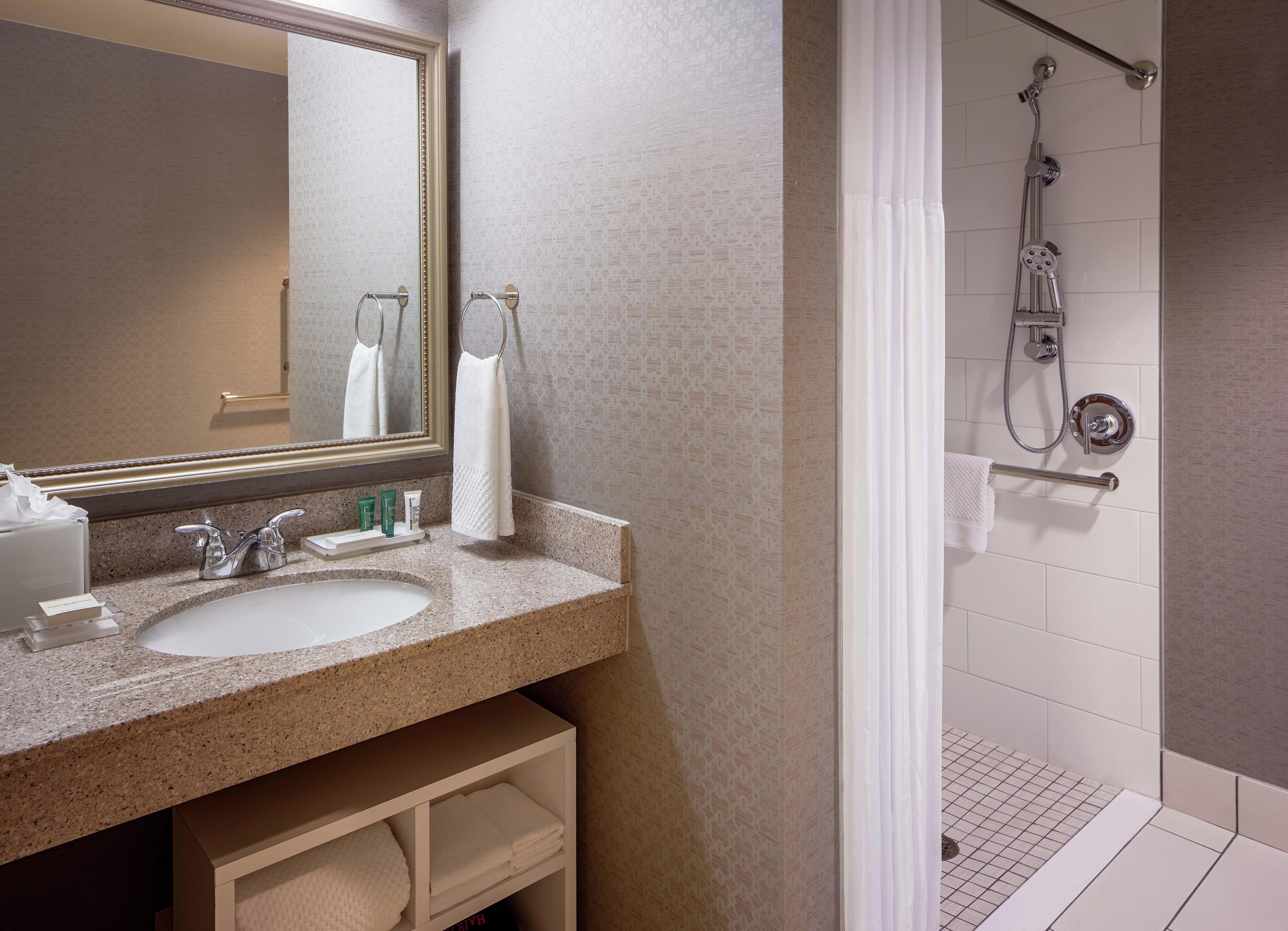 A hotel bathroom with a double sink, a large mirror, a shower area, and a towel rack.