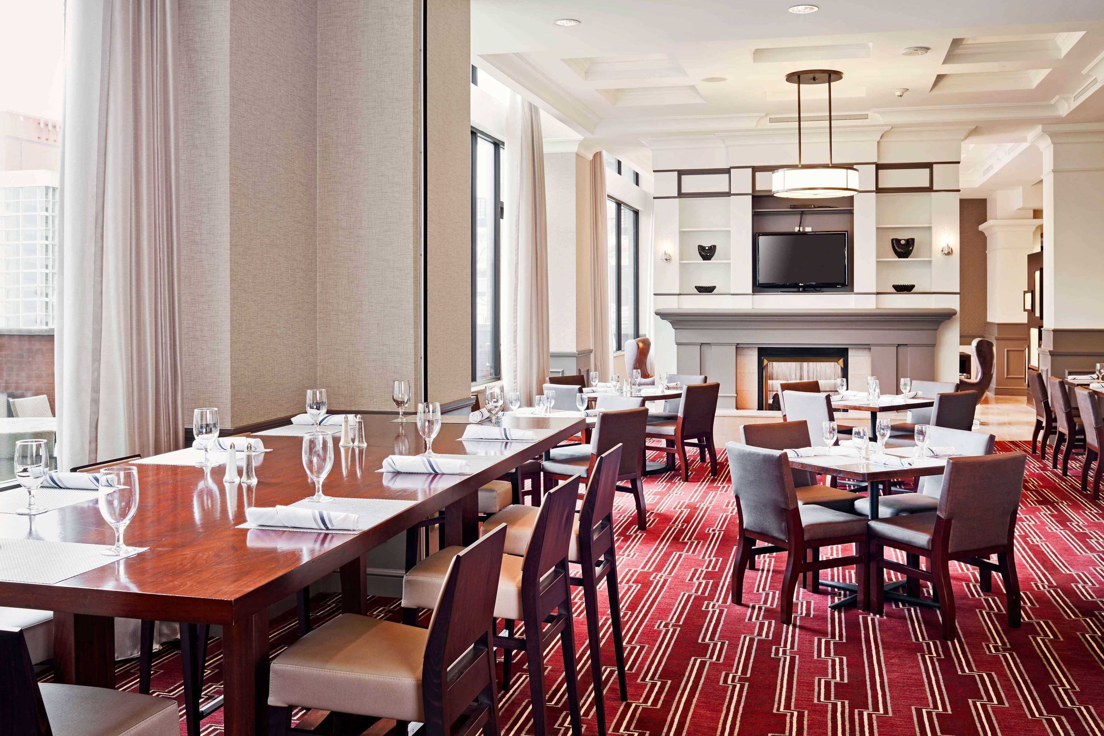 A hotel dining area with multiple tables, chairs, and a television mounted on the wall.