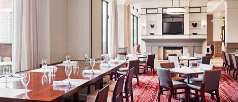 A hotel dining area with multiple tables, chairs, and a television mounted on the wall.