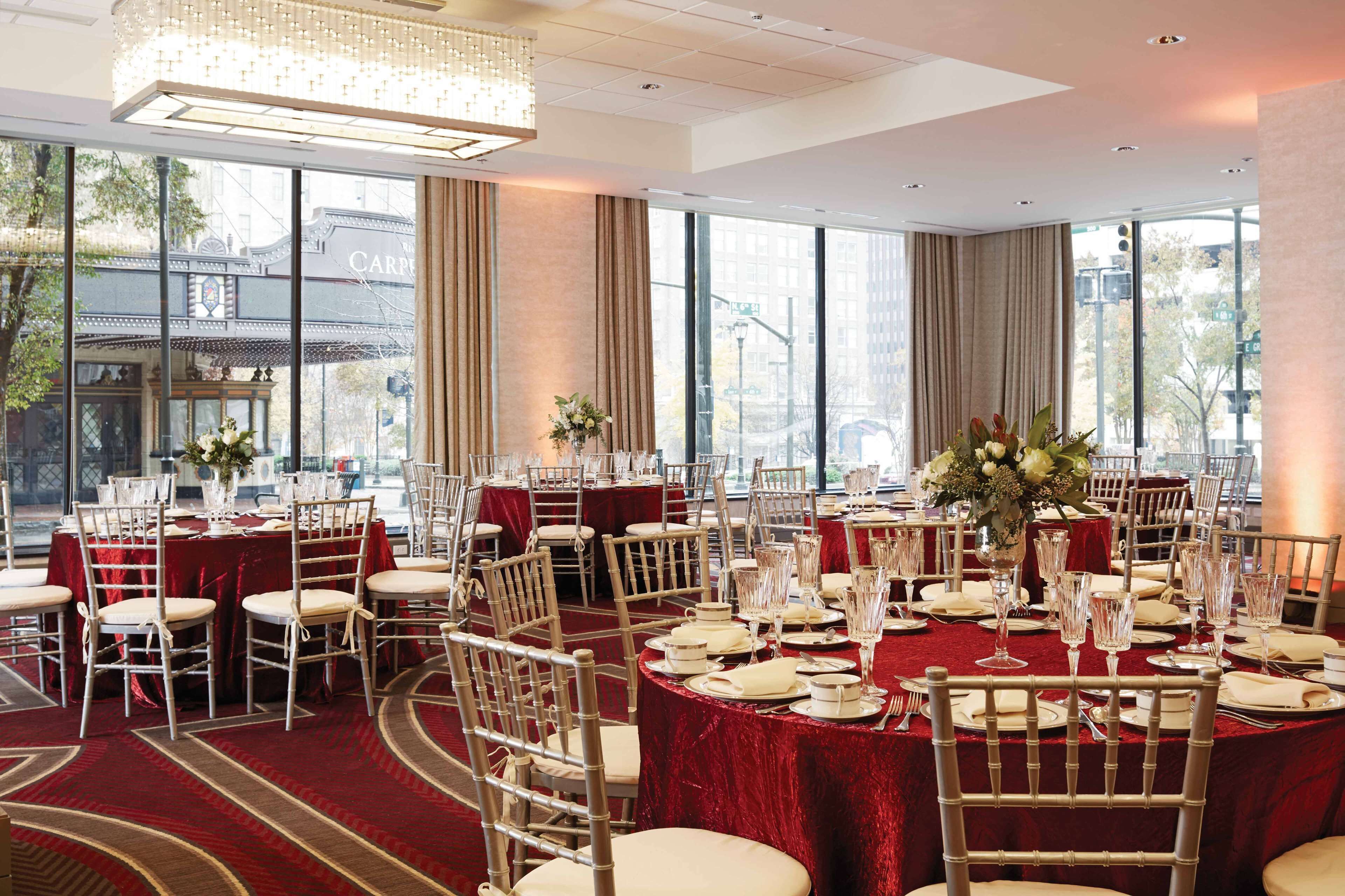A banquet hall with round tables set for dining, large windows, and a view of a building outside.