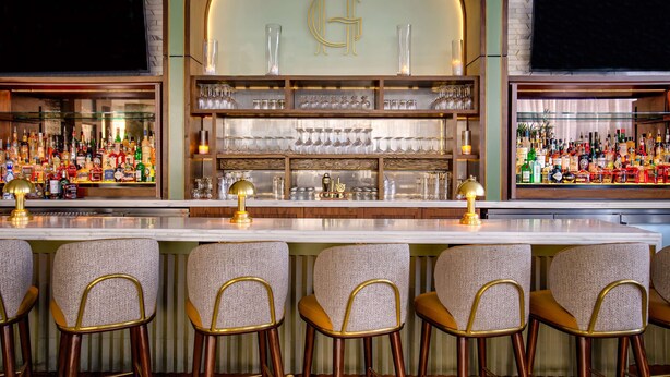 Un bar con mostrador de mármol, detalles dorados y una variedad de botellas de licor.