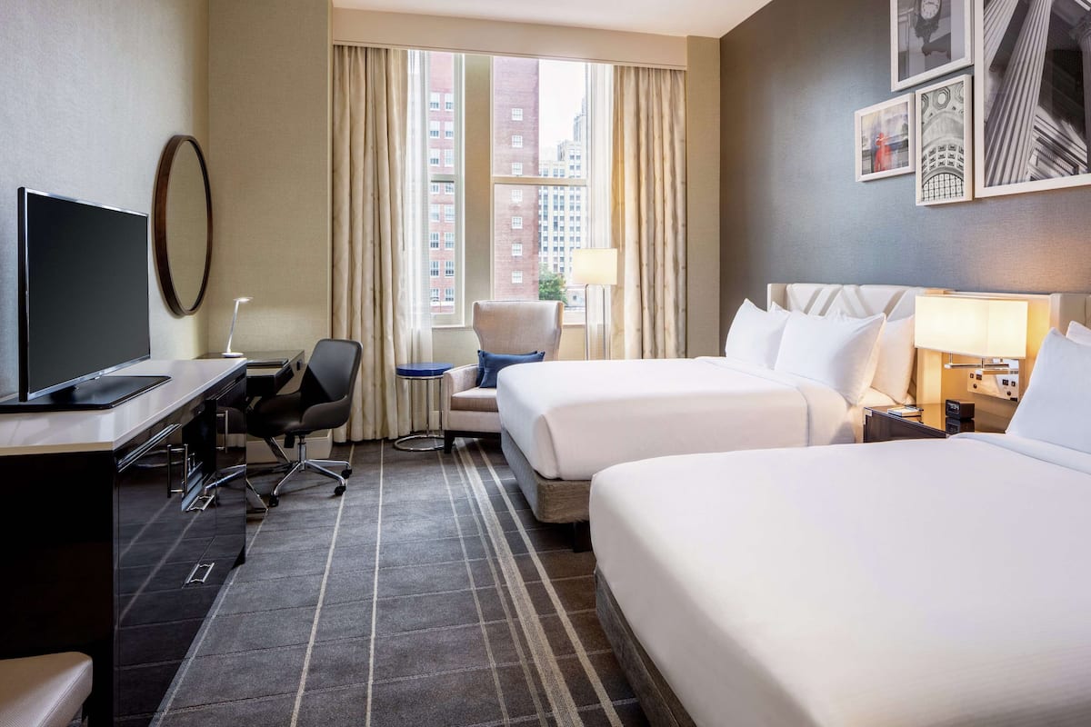 A hotel room with two beds, a desk with a laptop, a chair, a TV, and a window with curtains.