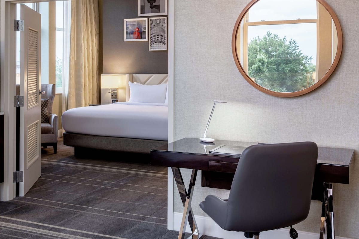 A hotel room with a bed, desk, chair, and a round mirror.