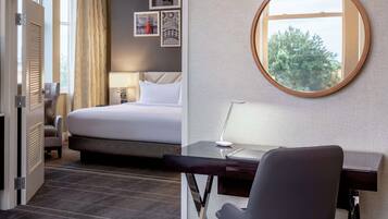 A hotel room with a bed, desk, chair, and a round mirror.