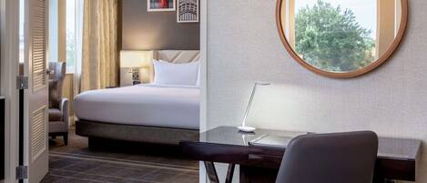 Habitación de hotel con cama, escritorio, silla y espejo redondo.