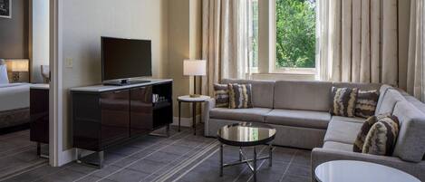 A hotel room with a sofa, a TV, a small table, and a cabinet.