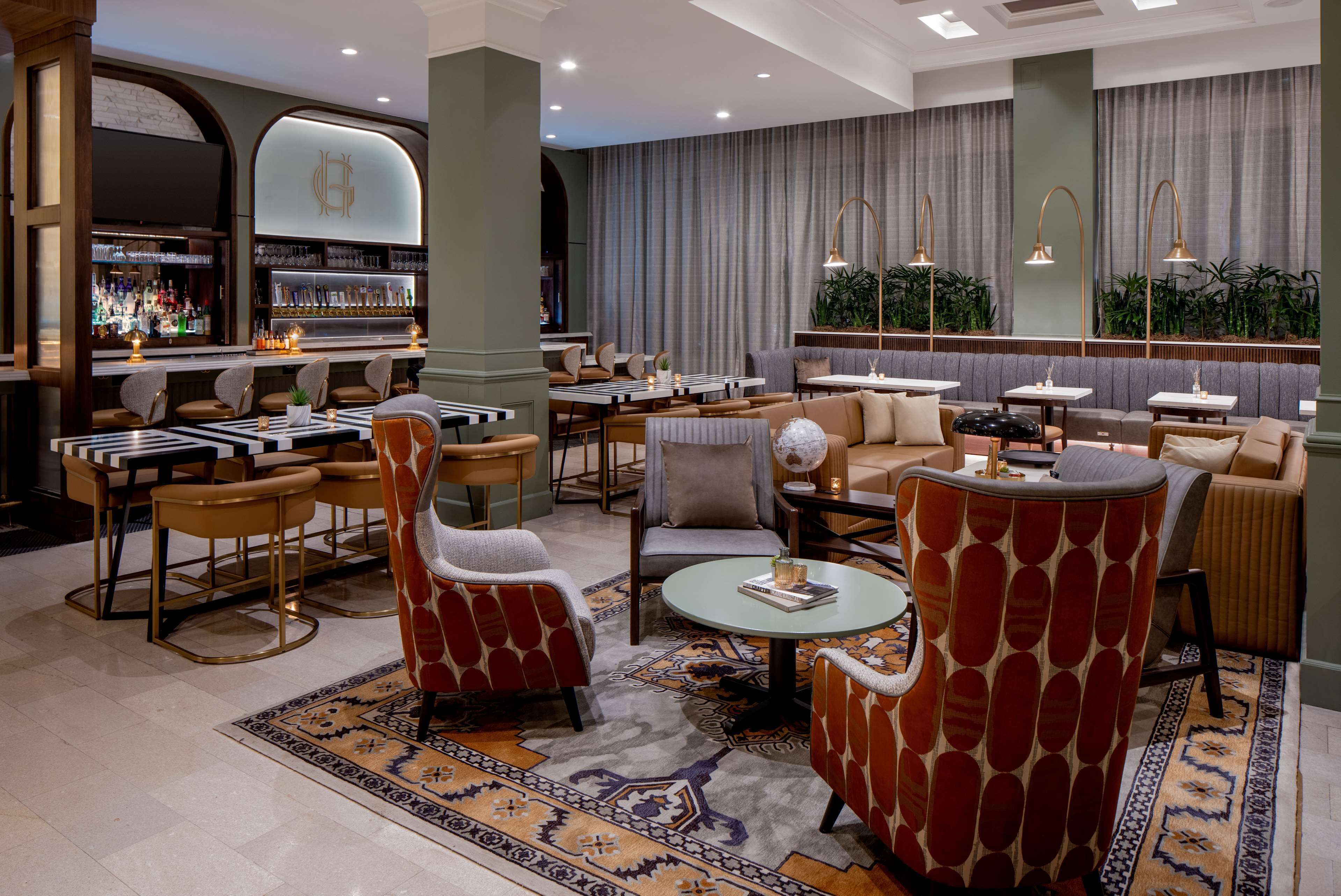 A spacious lounge area with multiple seating options, a bar with a variety of bottles, and a large window with curtains.