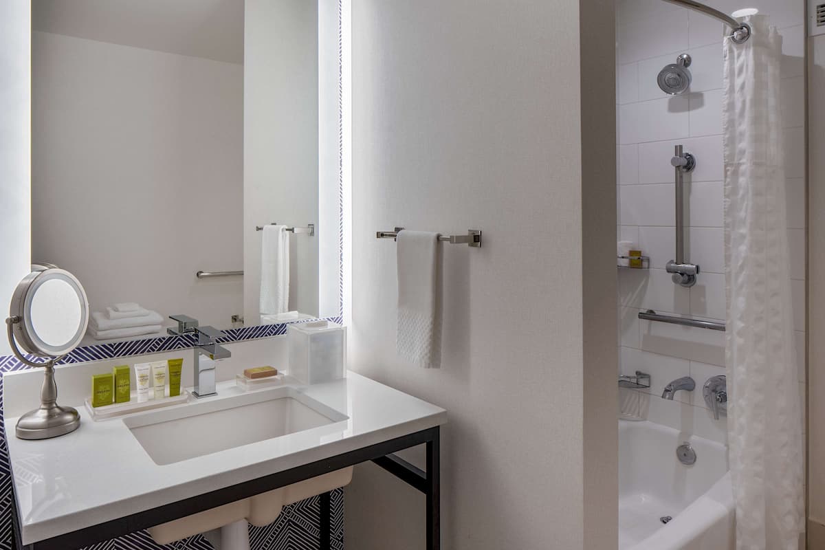 A bathroom with a white sink, mirror, and shower. There are towels and toiletries on the counter.