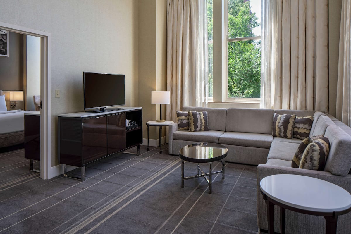 A modern hotel room with a sofa, a television, a small table, and a cabinet.