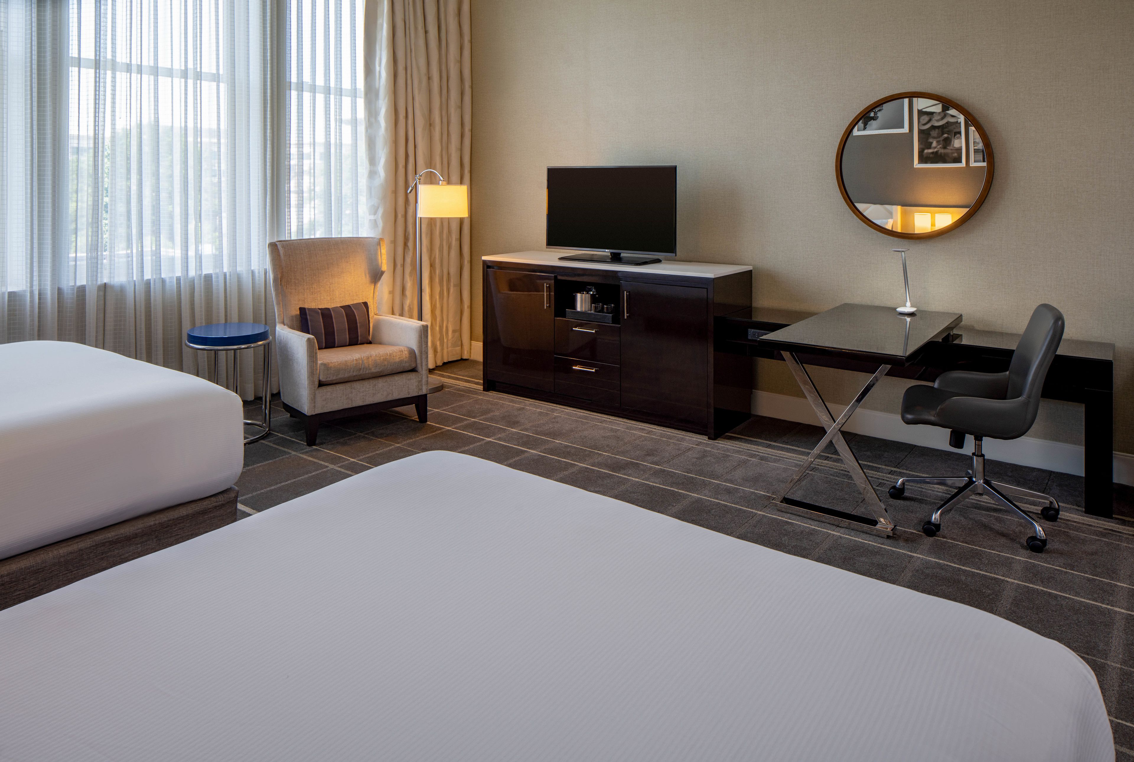 A hotel room with a bed, a desk, a chair, a television, and a mirror on the wall.