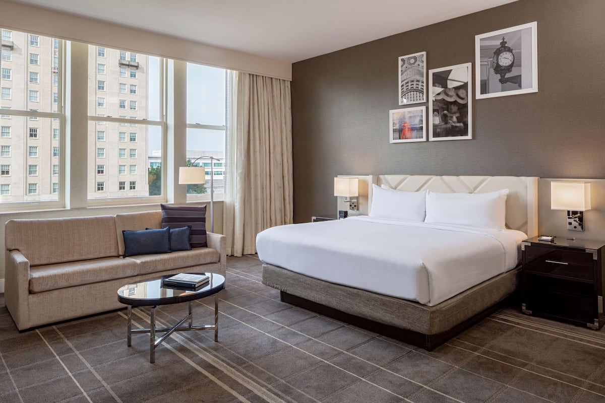 A hotel room with a large bed, a sofa, a small table, and a nightstand.