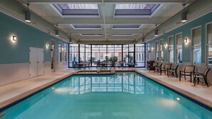 Una piscina interior con techo de cristal, zona de estar y vistas al exterior.