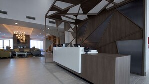 Een moderne receptiezone met een houten receptiebalie, zithoek met banken en een kroonluchter.