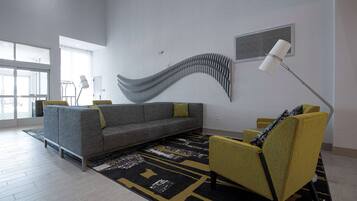 Una sala de estar moderna con un sofá gris, un sillón amarillo y una alfombra negra y amarilla con estampado.